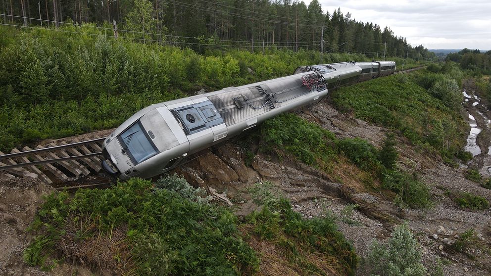 Ett tåg har spårat ur och lutar ner mot en slänt.