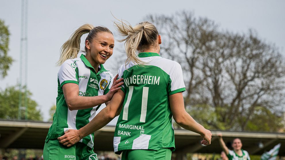 Fotbollsspelare i gröna och vita tröjor firar mål på en utomhusarena med publik.