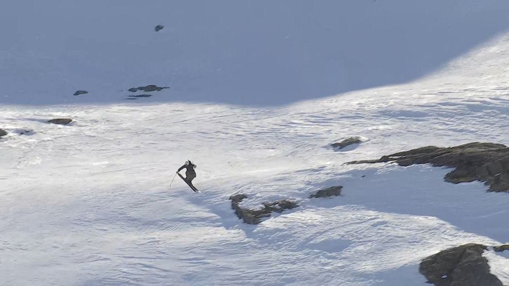 Ensam skidåkare åker nerför en snötäckt bergssida med klippor och skuggor.