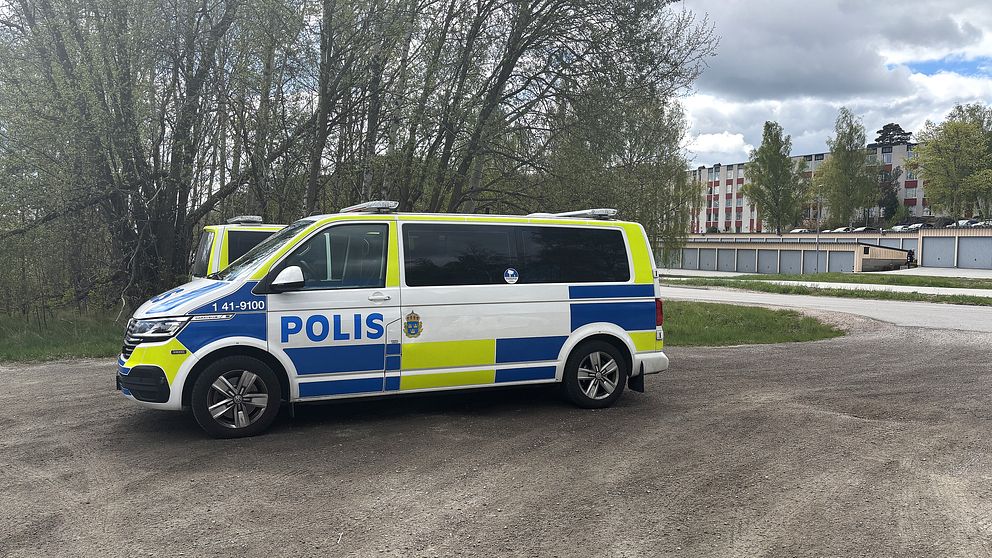 En svensk polisbil står parkerad vid en väg nära träd och en bro över vatten.