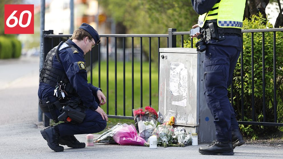 Två poliser vid ett blomhav på trottoaren, minnesplats efter händelse utomhus.