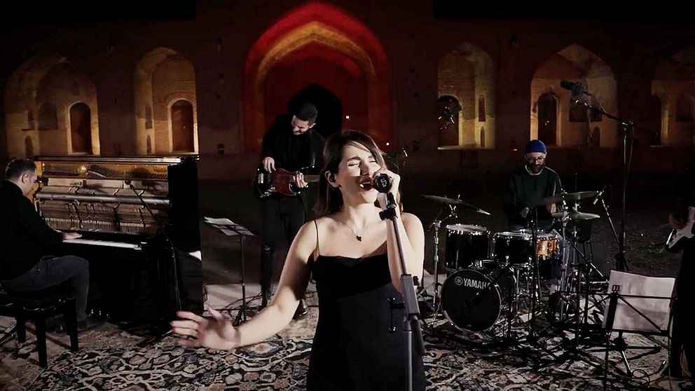 Parastoo Ahmadi i Iran framträder på en scen utomhus, omgiven av en pianist, en gitarrist och en trummis. Bakgrunden har vackert upplysta bågar och väggar.