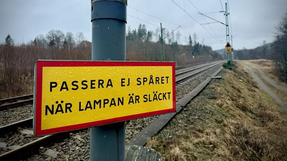 Varningsskylt vid järnvägsspår med text ”Passera ej spåret när lampan är släckt”.