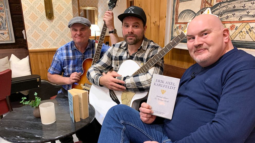 Tre av medlemmarna i Larz Kristerz sitter i en soffa. Två av dem håller instrument i händerna, den tredke en bok av Erik Axel Karlfeldt.