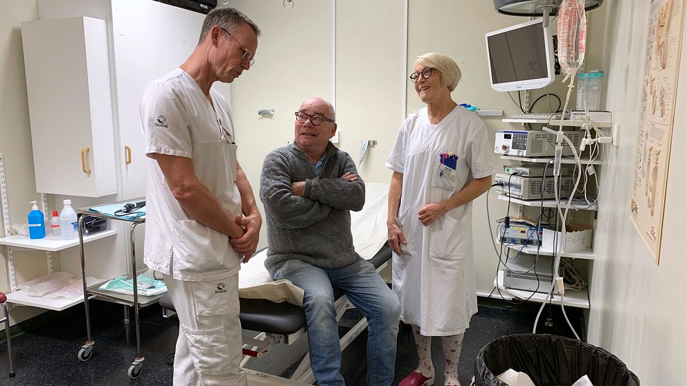 Tre personer, en läkare, en sjuksköterska och en patient står och snackar i ett besöksrum.