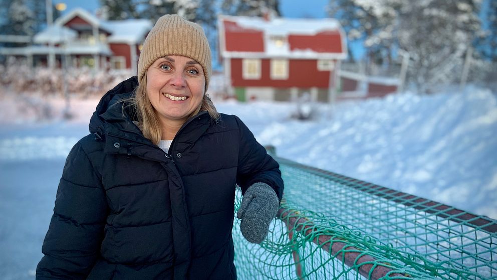 Kvinna med vinterkläder lutar sig mot ett hockeymål på en isbana.