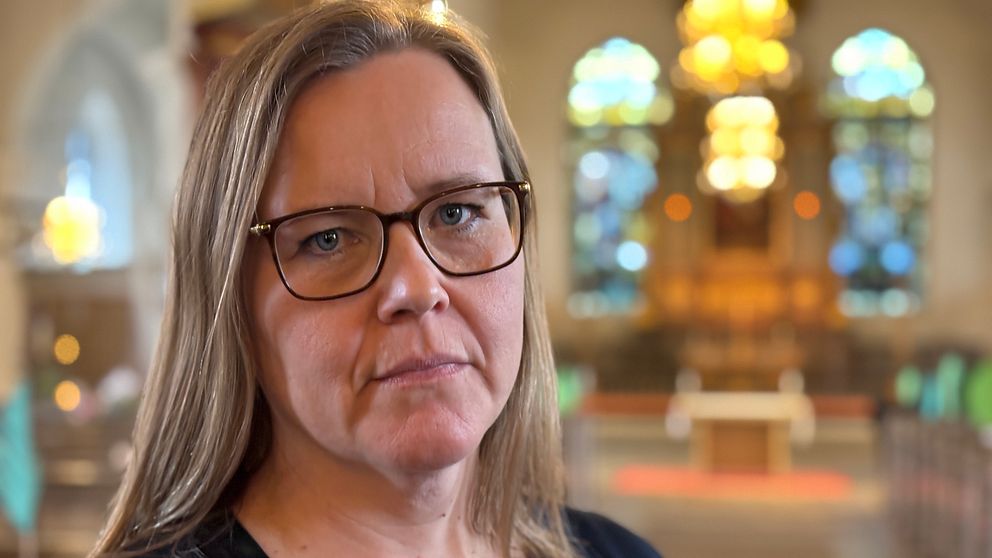 Person i kyrkointeriör, altar bakgrund upplyst, sittplatser på båda sidor.