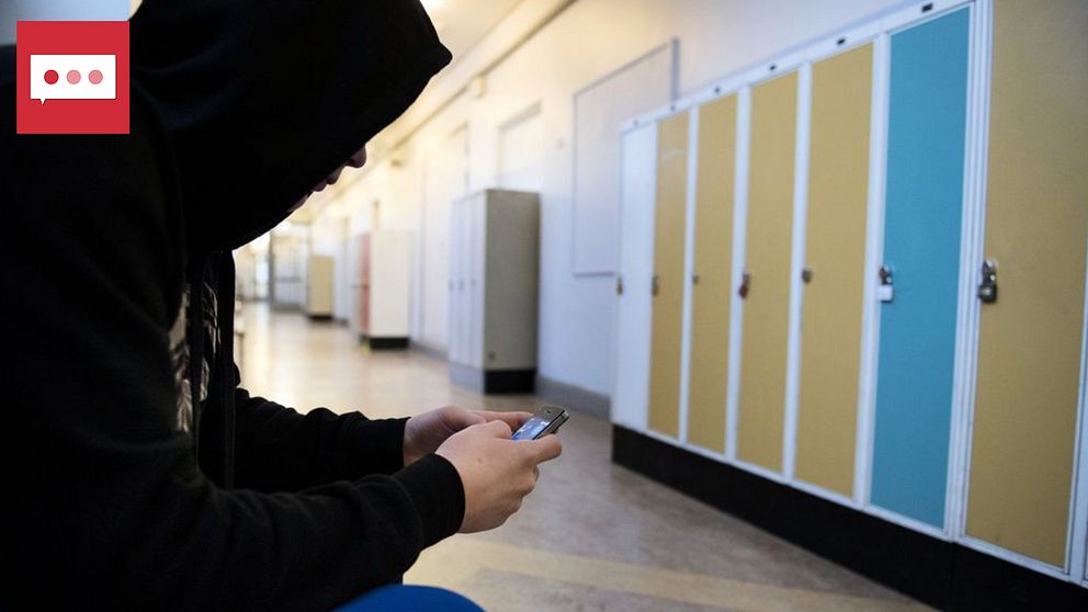 En anonym tonåring håller på med mobilen i en skolkorridor.