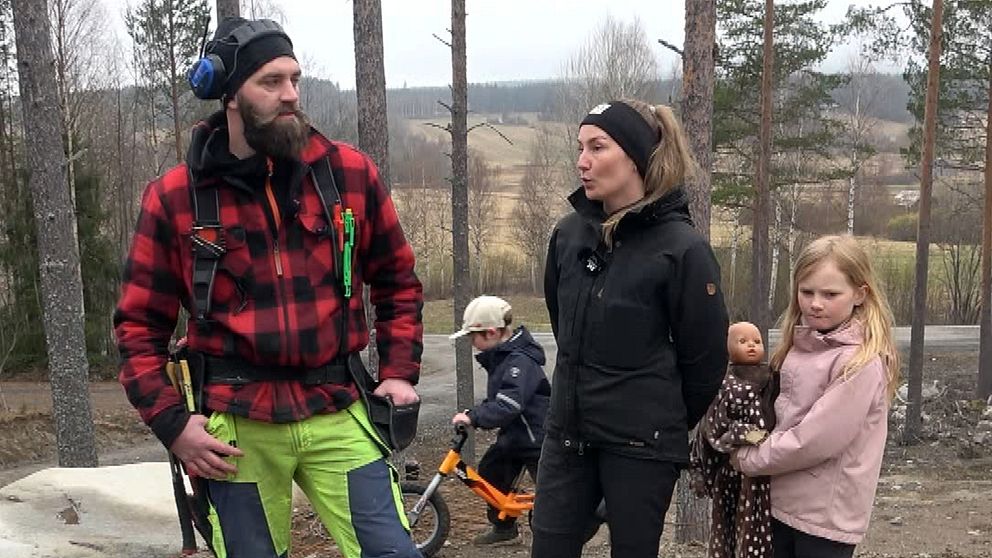 Fyra personer utomhus i skog, ett barn håller docka, ett annat barn sitter på cykel.