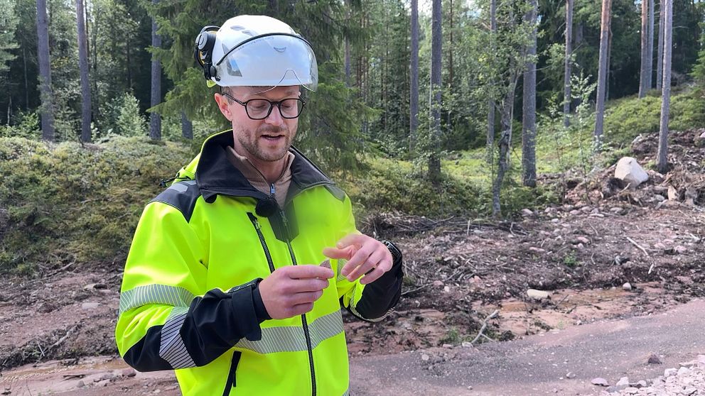 man i varselkläder och bygghjälm står och pekar på en vass sten