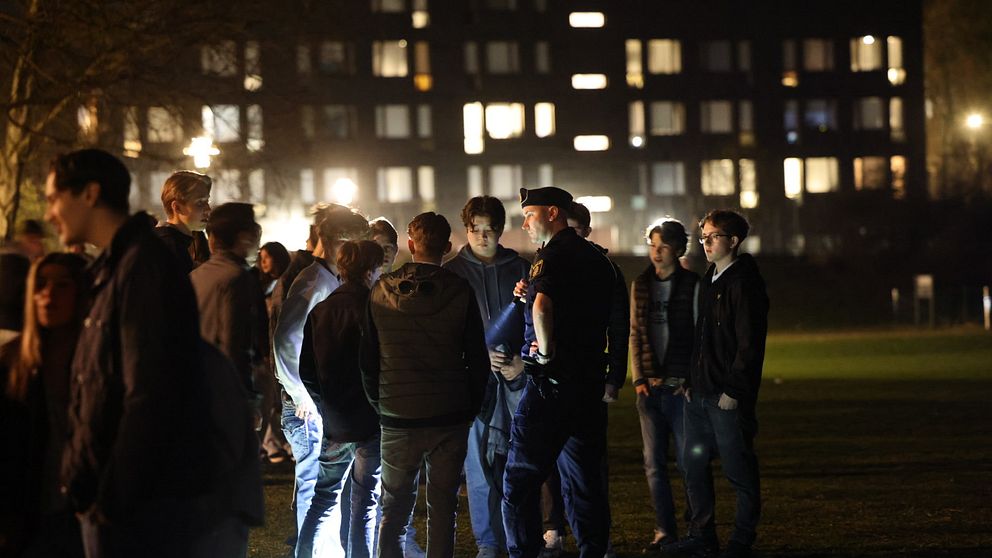 En polis står med ficklampa vid en stor grupp ungdomar på Hoppbacken i Enskede under valborgsnatten.