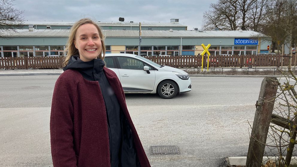 Petra Ahlman står vid väg med korsande vit bil och skolbyggnad i bakgrunden.
