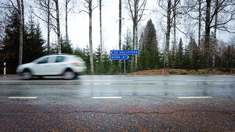 En bil åker snabbt förbi i Stadra. En skylt med Hällefors åt ena hållet och Nora åt andra.