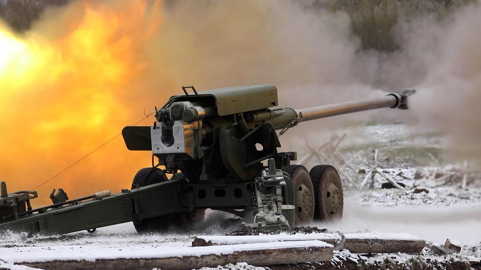 Artilleri avfyrar med eld och rök i bakgrunden på ett snötäckt fält.