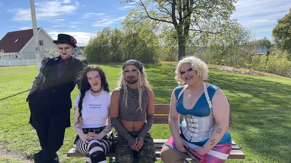 Fyra personer med alternativa klädstilar sitter utomhus på en bänk i en park.