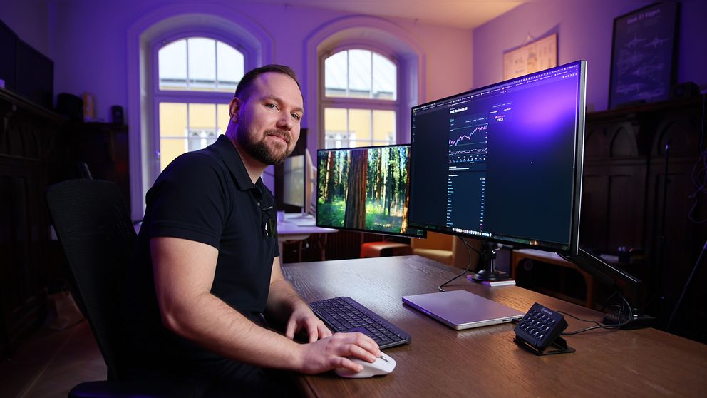 Person vid skrivbord med flera datorskärmar som visar grafer och data.