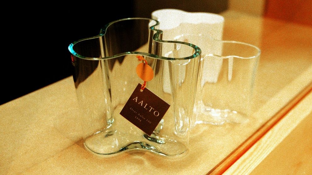 Tre vaser av glas i olika former står på en yta. Den största vasen är medelstor och har en unik, böljande design med en prislapp som visar ”AALTO”. De andra två är mindre, mer traditionella glasvaser i enkelt utförande.