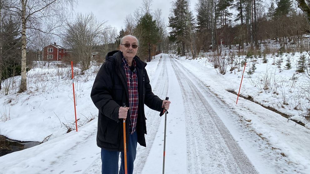En man står med stavar på en snöig grusväg