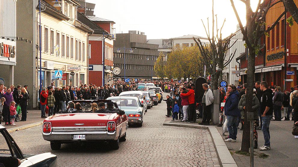 Bilkorteg med veteranbilar kör genom stadsgata, åskådare står längs trottoarerna.