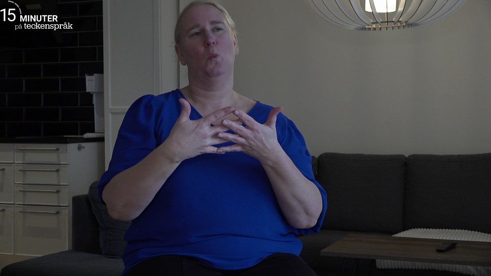 Mona Riis i blå tröja sitter i ett vardagsrum och tecknar ordet blå.