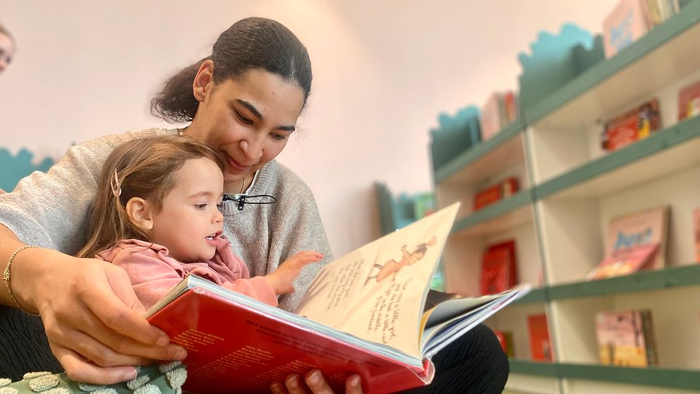 Mamma Sandy Heijbel sitter och läser en bok på biblioteket med Amacia 3 år.