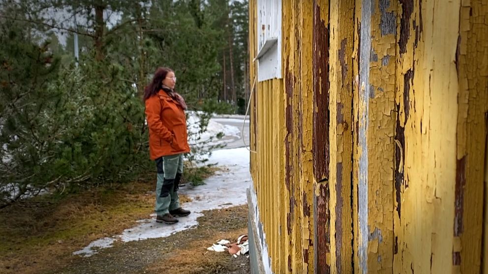 Kvinna står vid ett färgflagat gult hus.