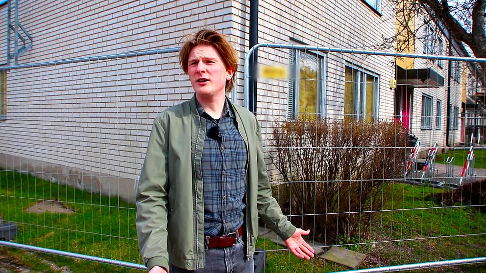 En ung man står framför en instängslad byggnad