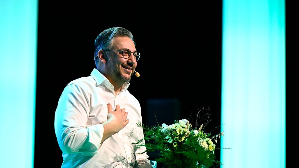 Muharrem Demirok i vit skjorta talar på Centerpartiets scen och håller en blombukett.
