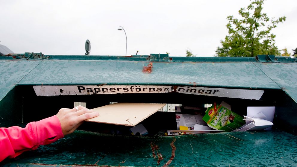 Källsortering. En person stoppar in papper i en container.