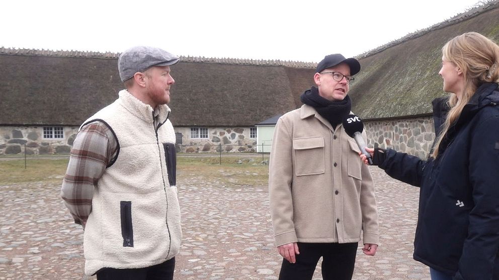 Reporter intervjuar två personer utomhus på en gårdsplan till Slottslängorna i Sölvesborg. De står på kullersten.