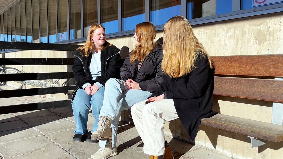 tre unga tjejer sitter på en bänk utomhus.