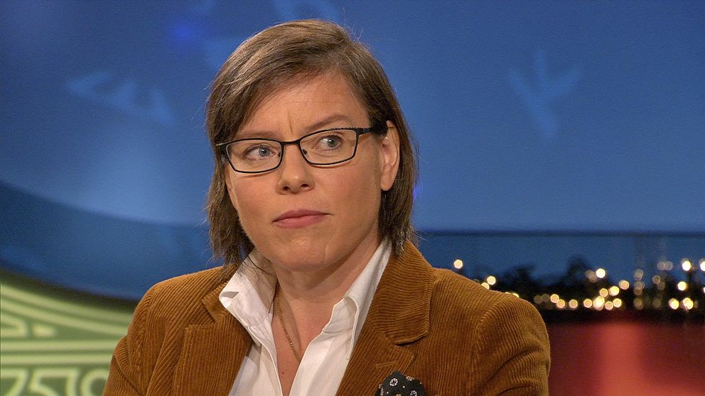 Person i brun kavaj mot bakgrund av stadsljus och blå himmel vid en studie.