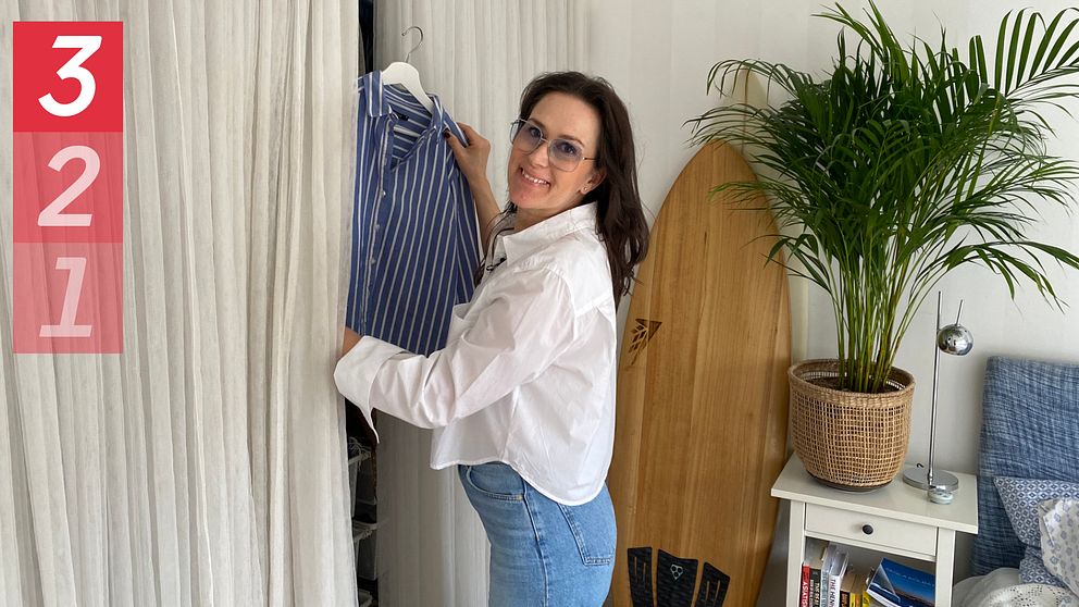 Bild på kvinna i jeans och vit skjorta som lyfter ut en randig skjorta på en galge från en garderob.