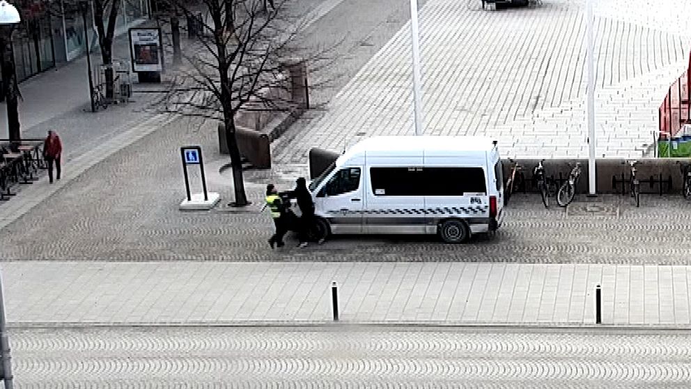 Två personer knuffas nära en vit skåpbil på en tom gata i stadsmiljö.