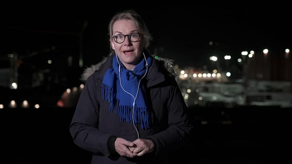 Person i mörk jacka och blå halsduk med nattlig stadsmiljö i bakgrunden.
