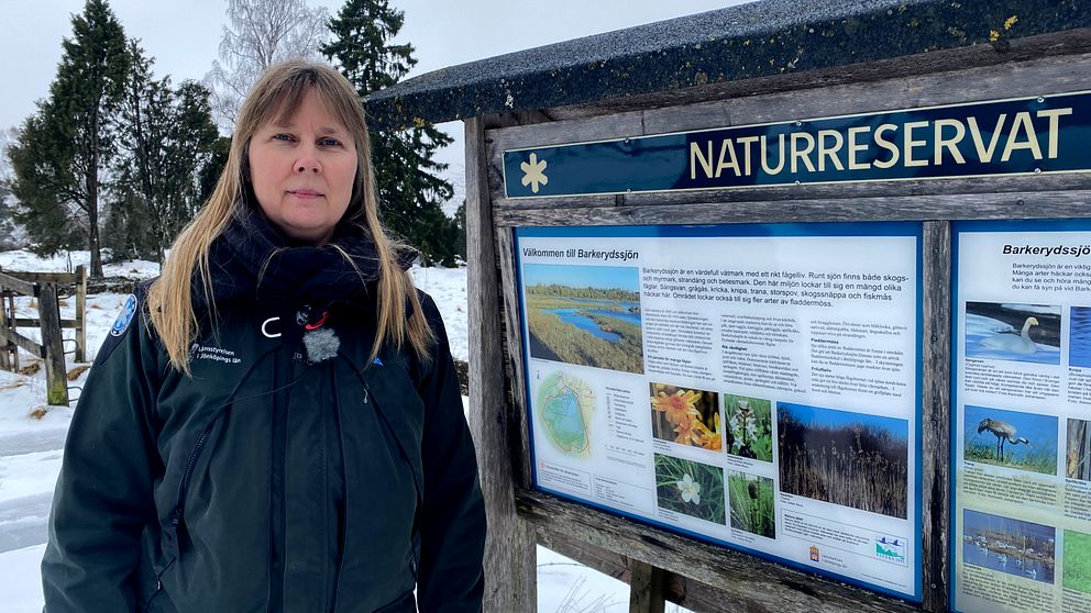 Eva Wallander, enhetschef naturvårdsförvaltningen länstyrelsens jönköping, kvinna med ljust hår och blå jacka står vid en naturreservatsskylt vid Barkerydssjön