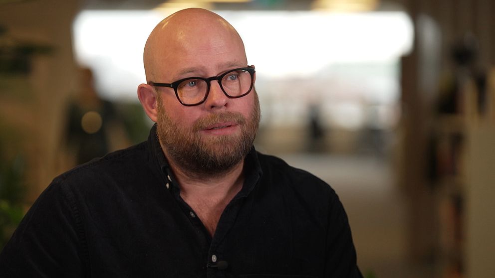 Fotograf Anders Hansson sitter i en korridor, klädd i en mörk skjorta. Bakgrunden är oskarp.