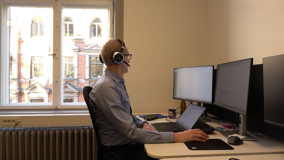 en man sitter med ett headset framför tre dataskärmar
