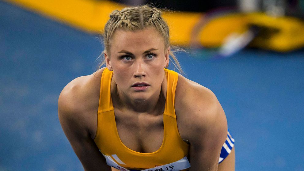 Atlet i sportdräkt står lutad med händerna på knäna på en löparbana.