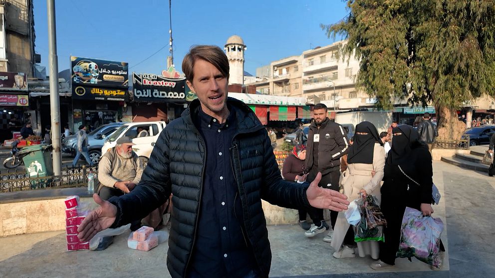 Tomas Thorén står med utsträckta armar på en livlig marknadsplats, omgiven av människor som bär på kassar. I bakgrunden syns affärer och ett minaret.