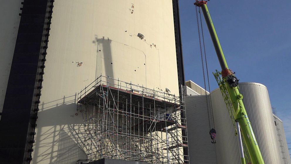 En byggnadsställning som står intill en hög vägg på Ringhals. En kran används för att lyfta material eller utrustning, medan arbetare syns i närheten.