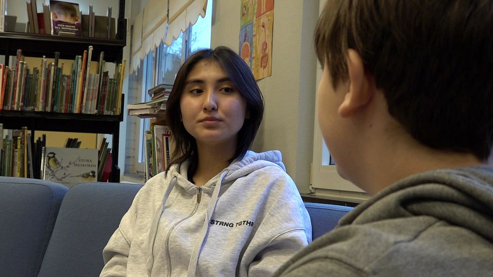 Två elever sitter i en soffa, en har ryggen mot kameran. De sitter bredvid en bokhylla.