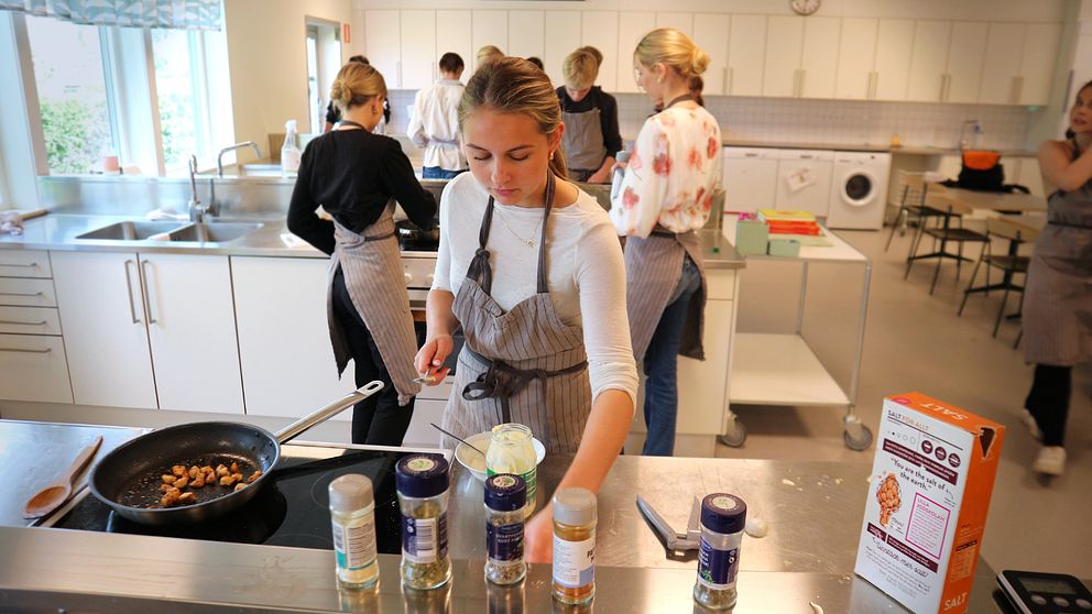 Ungdomar lagar mat tillsammans i ett skolkök, flera kryddburkar syns på bänken.
