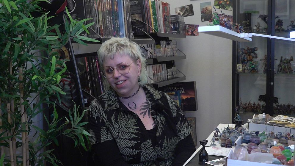 Lovisa Falk sitter bland spel och böcker i spelbutiken i Falun. Hon ha blont hår, glasögon och en bladmönstrad skjorta.