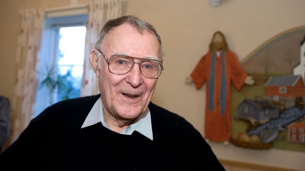En äldre person sitter i ett rum med religiös konst och ett fönster i bakgrunden.