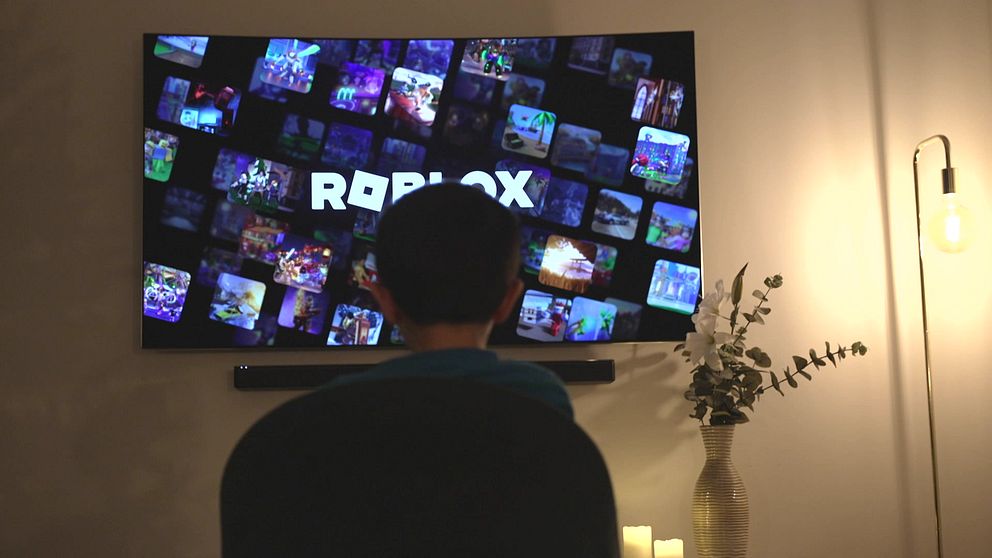 Ett barn sitter framför en stor TV som visar en mängd olika miniatyrbilder från spelet Roblox.