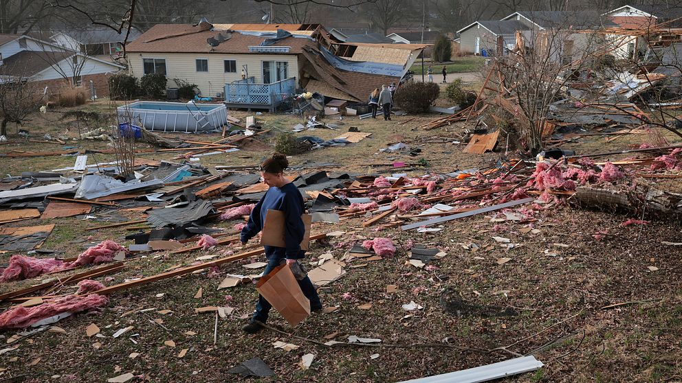 Man går genom förödelse av förstörda hus efter en tornado i en bostadsområde.