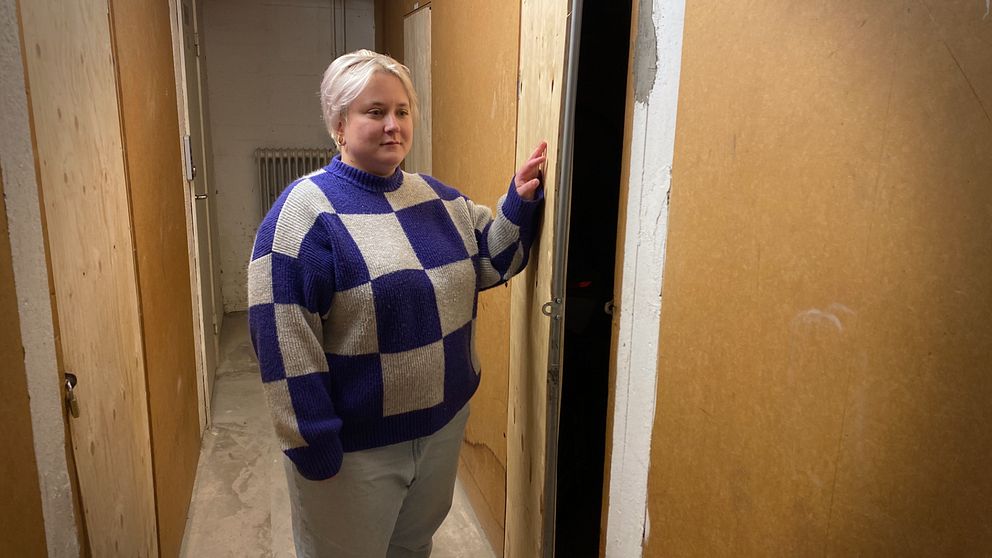 Kvinna står i rutig stickad tröja i en korridor mellan lägenhetsförråd.