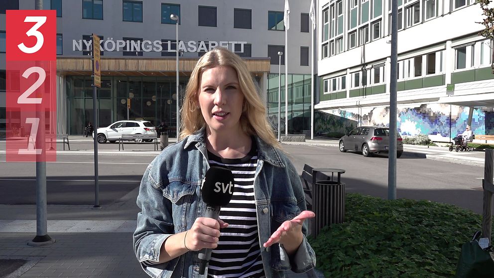 SVT:s reporter Frida Grunnvald står utanför Nyköpings lasarett med en mikrofon och är vänd mot kameran.