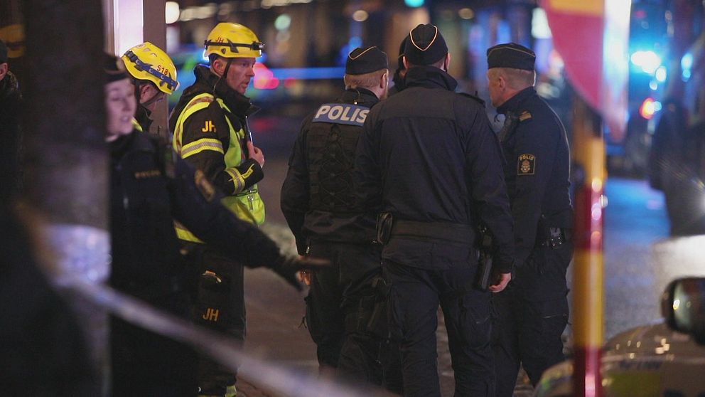 Poliser och brandmän utanför den brandhärjade byggnaden. Det är mörkt ute och i bakgrunden syns blåljus